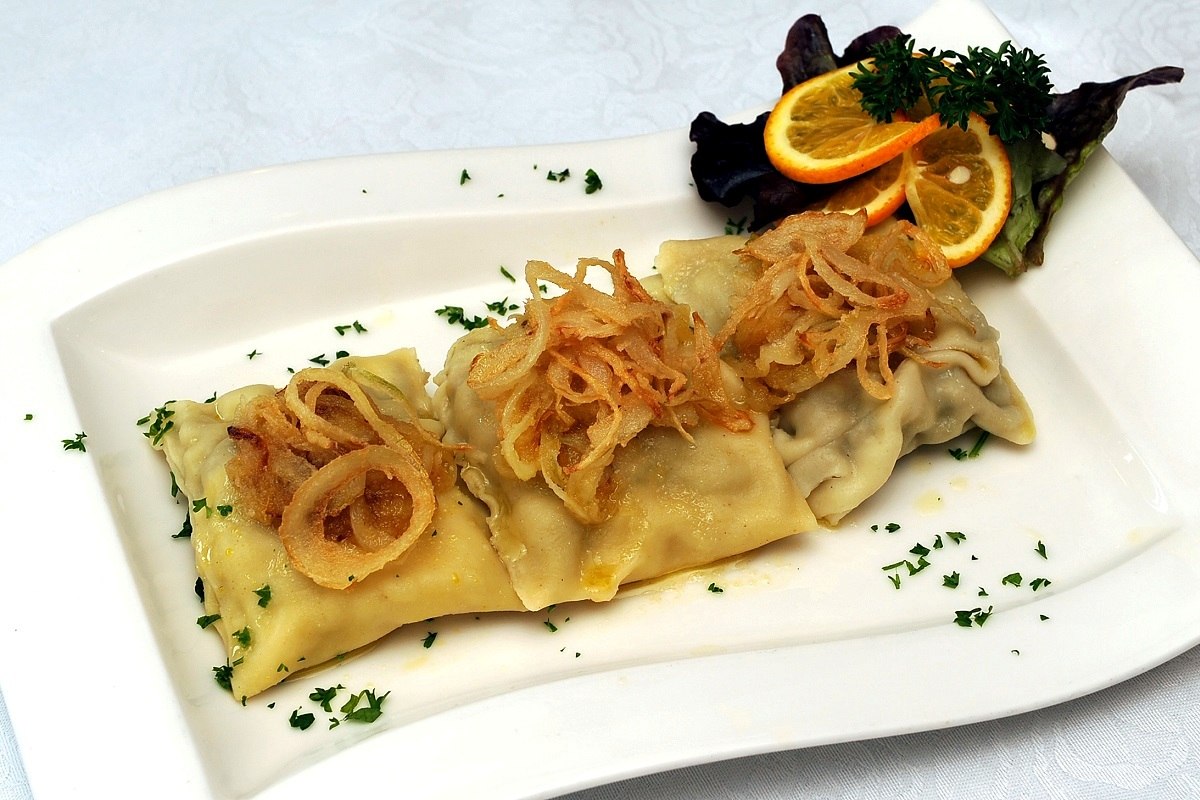 Geschmälzte Maultaschen auf einem weißen Teller, garniert mit Orangen und Schnittlauch