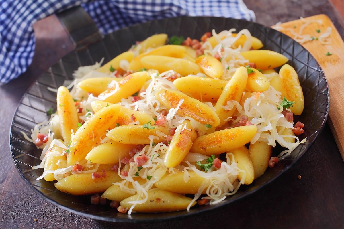 Eine Pfanne voller Schupfnudeln, die garniert sind mit Sauerkraut und Speck