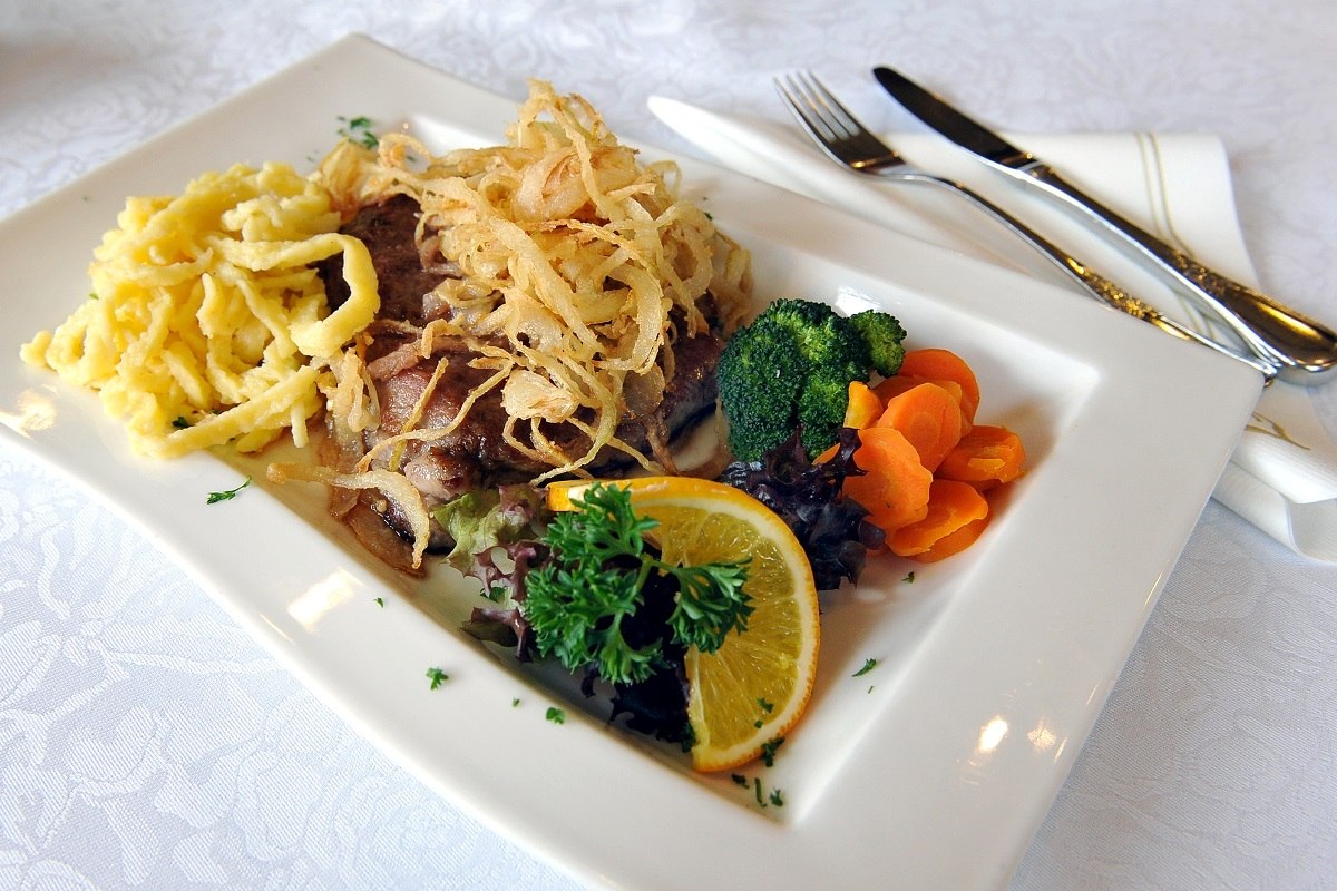 Schwäbischer Zwiebelrostbraten und Spätzle, garniert mit Zwiebeln, einer Orange und Karotten