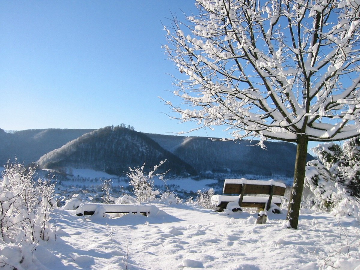 Verschneite Landschaft mit Bänkle und Blick auf den Burgberg und die Ruine Hiltenburg